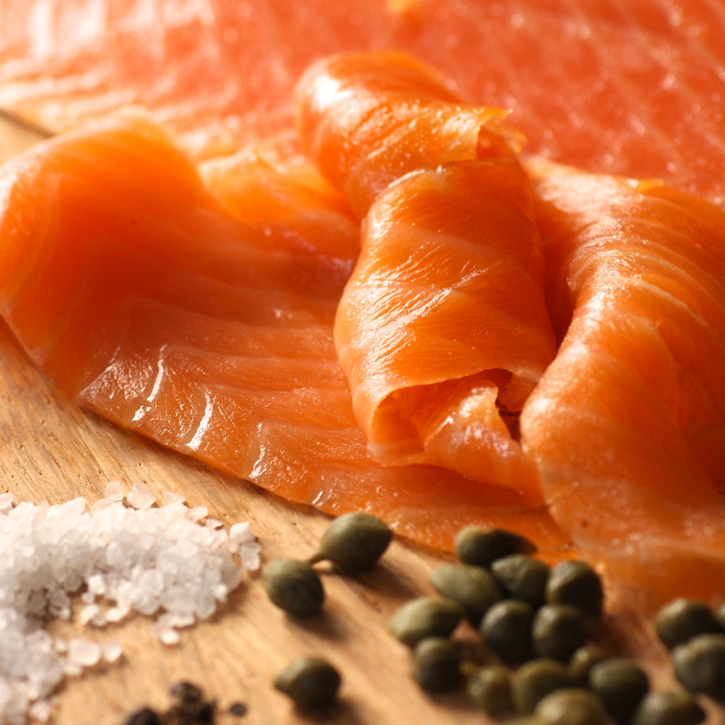 Smoked salmon slices on a wooden board with salt and capers.