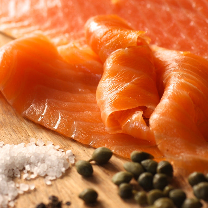 Smoked salmon slices on a wooden board with salt and capers.