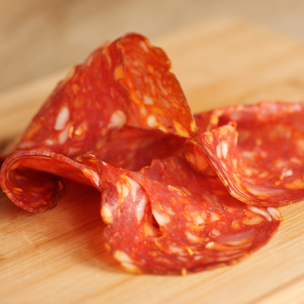 Slices of The Artisan-Smokehouse's smoked Spianata Calabra salami on wooden board