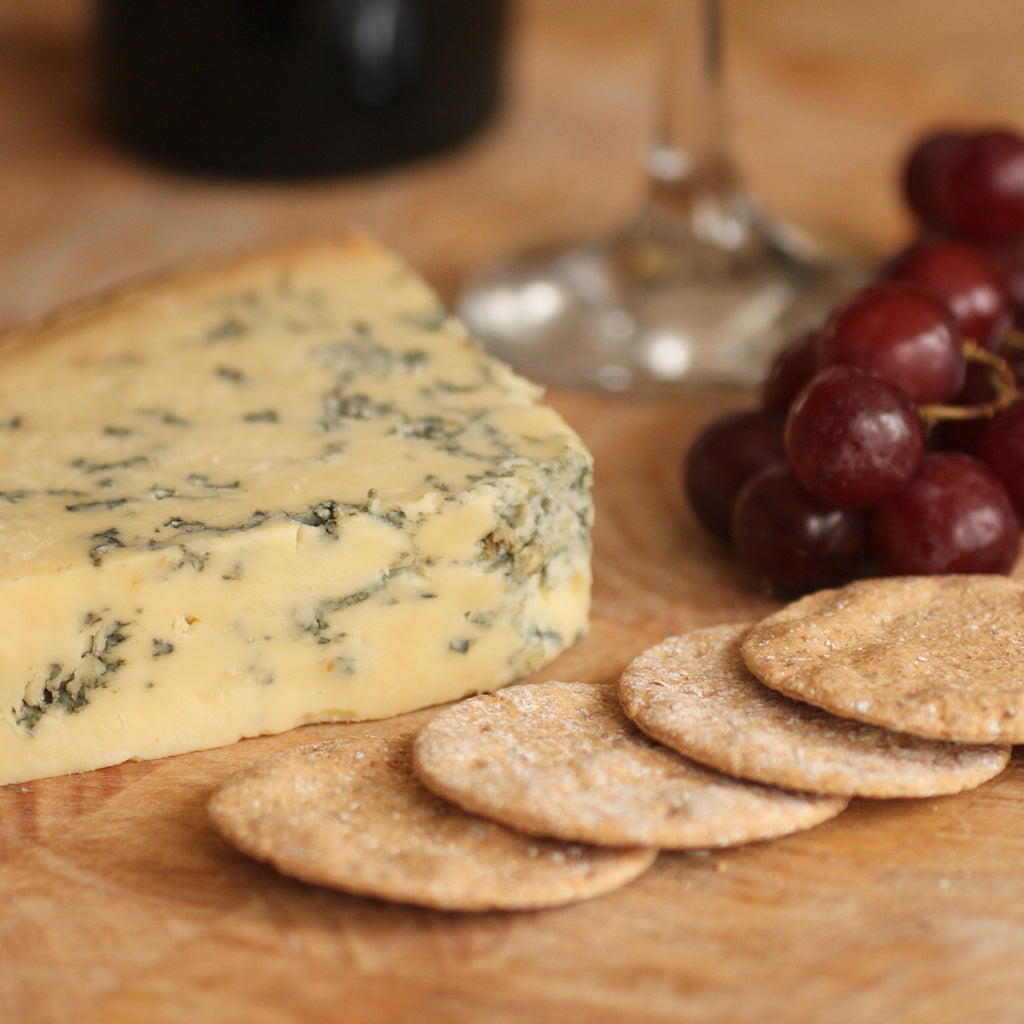 A piece of The Artisan Smokehouse's smoked Stilton on cheese board with wine, grapes and crackers
