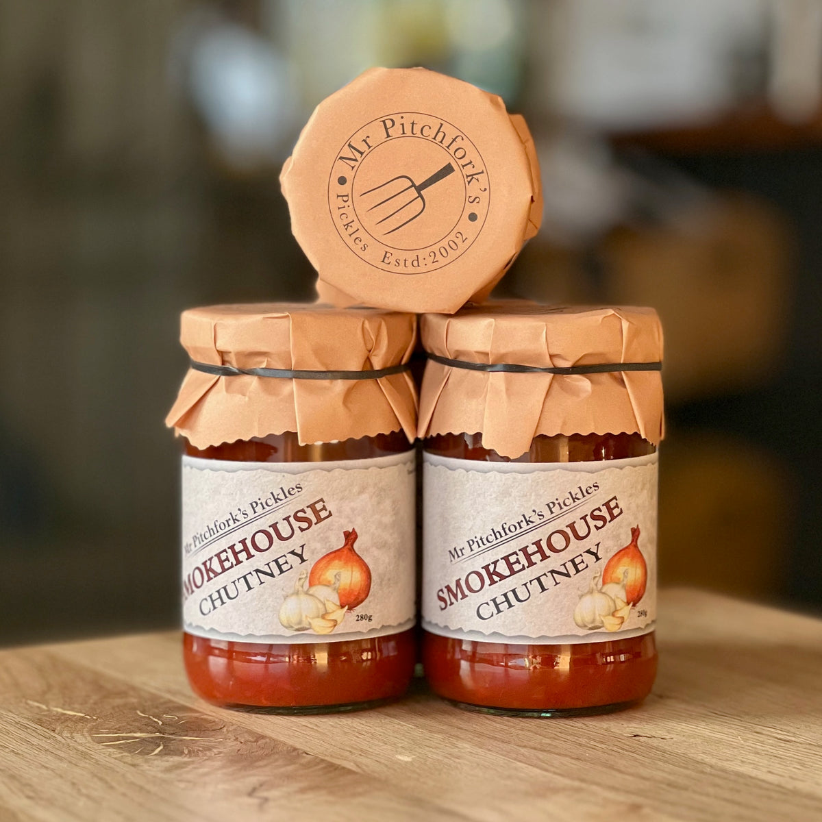 Two jars of Smokehouse Chutney with a third jar resting on top, displayed on a wooden surface.