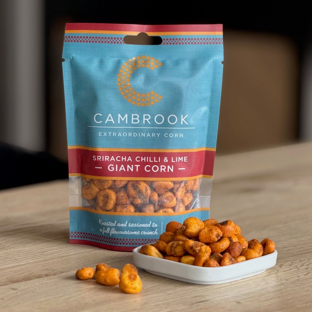 Packaged Cambrook Sriracha Chilli & Lime Giant Corn in a white bowl on a wooden surface.