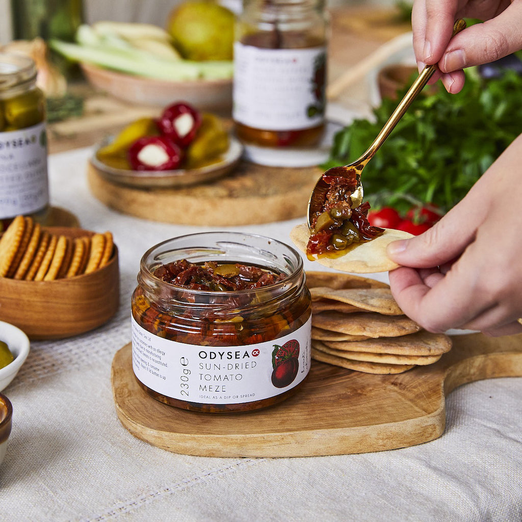 A jar of sun-dried tomato meze on board with crisp breads for dipping