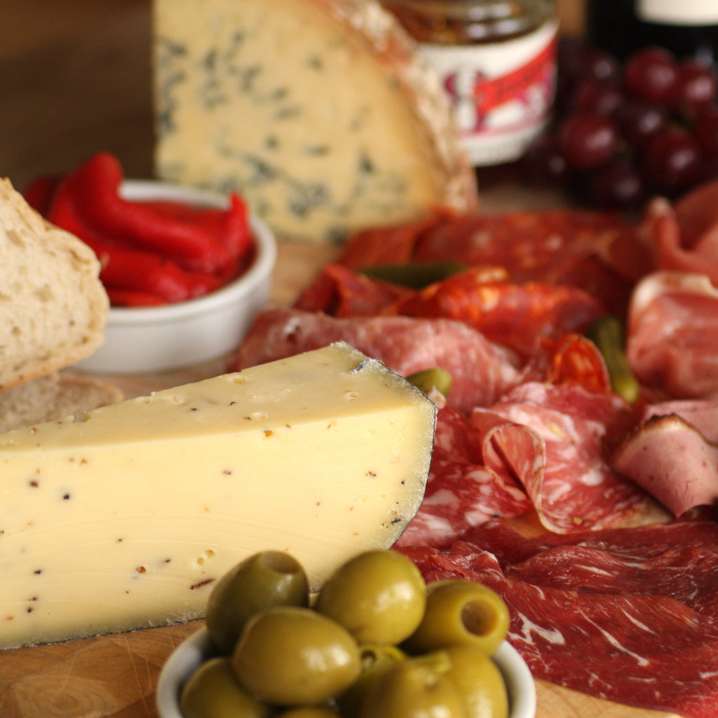 A piece of truffle Gouda on a cheese and meat platter with olives, chutney and grilled peppers