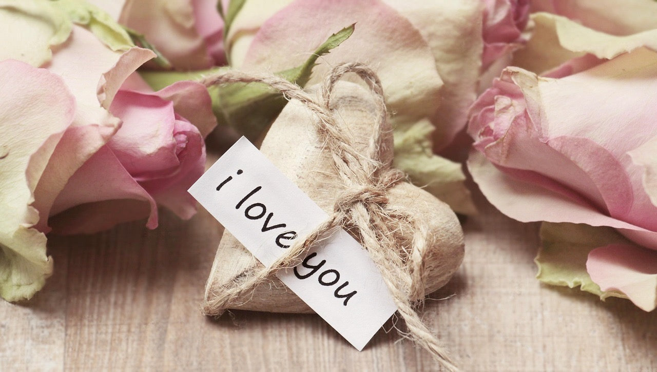 Pink roses with a small wrapped gift and 'I love you' card on a wooden surface
