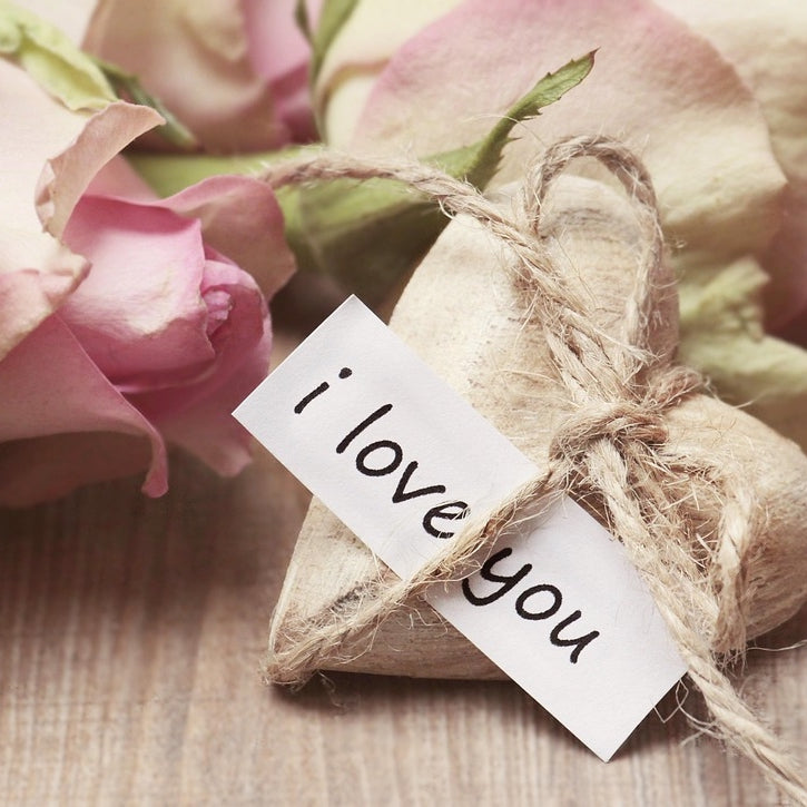 Bouquet of pink roses with a wrapped gift and 'i love you' card on a wooden surface.