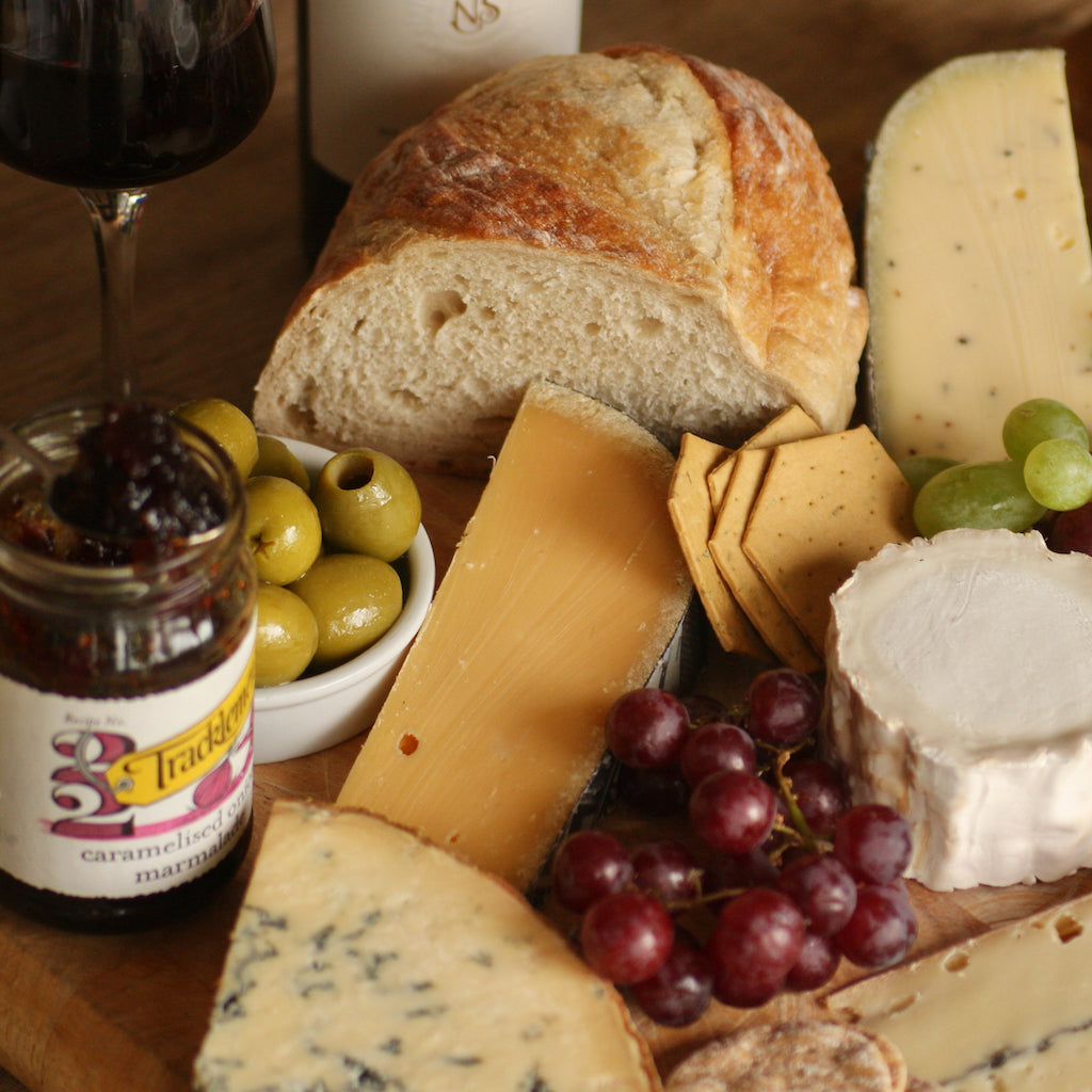 A piece of Weydeland Gouda on cheese board with grapes, smoked olives, crackers and chutney